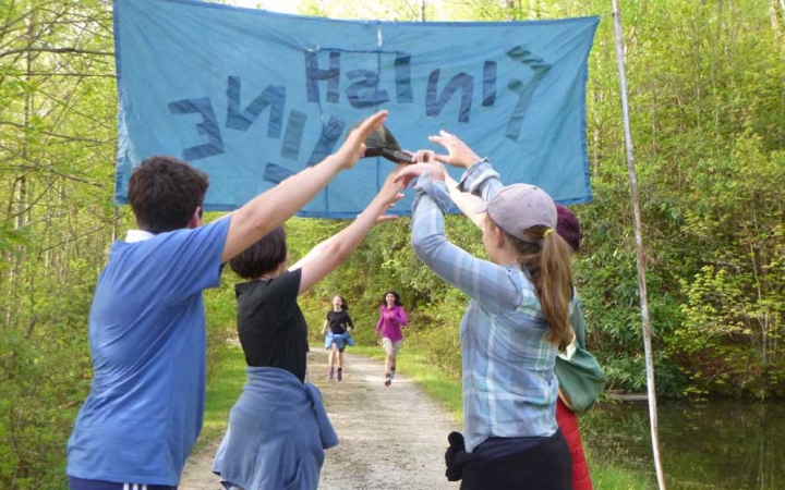 In the background, two students run forward toward a banner that appears to read "finish line." In font of the banner, four people make an archway with their lifted arms.